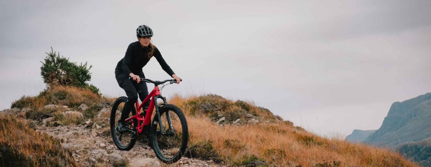 a woman riding a bike on a trail in the mountains