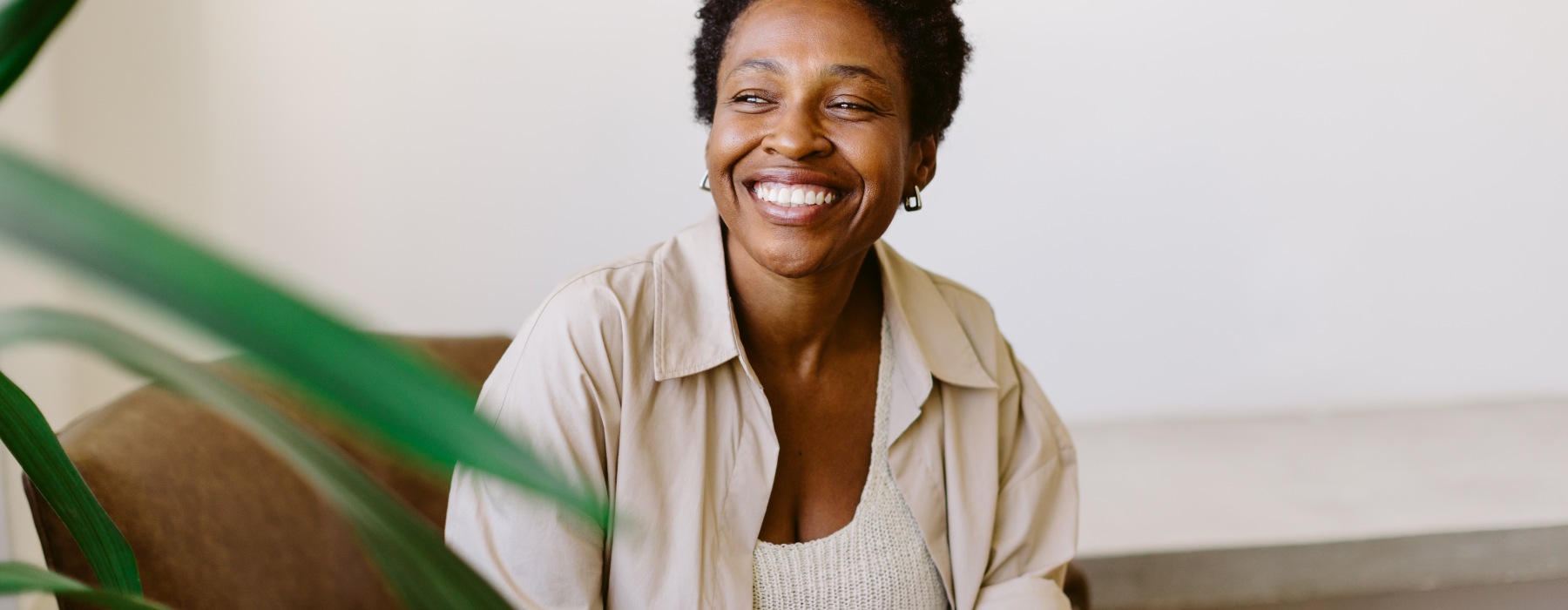 Person seated on a couch in a bright, modern living area, holding a smartphone, with neutral décor and indoor greenery in the foreground.